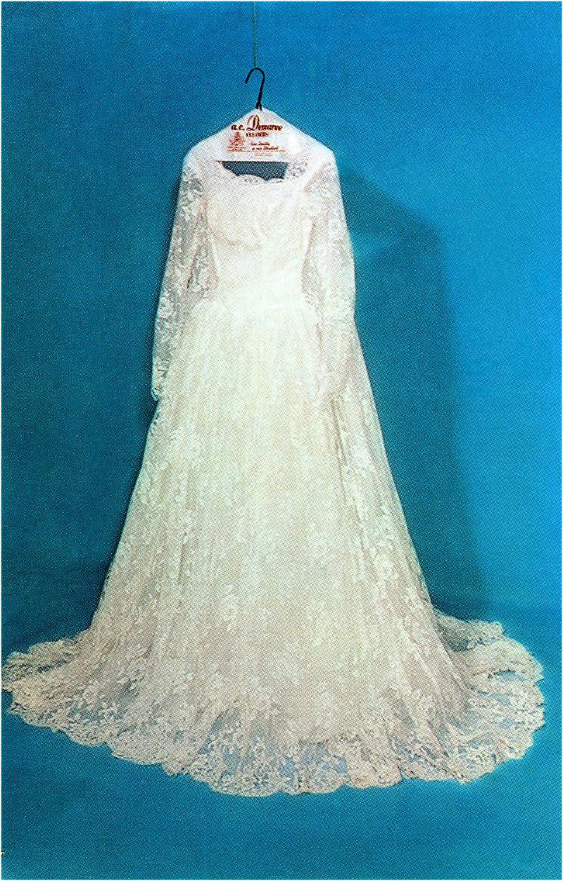 An old lace wedding dress hung up against a blue background.