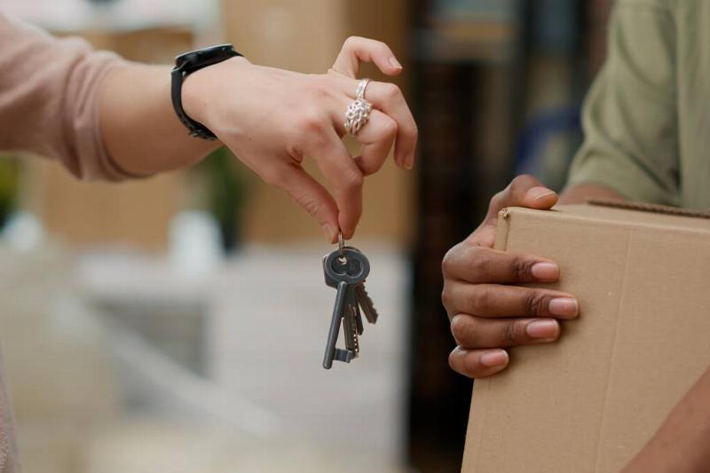A hand holding a set of house keys, passing them to someone holding a box.