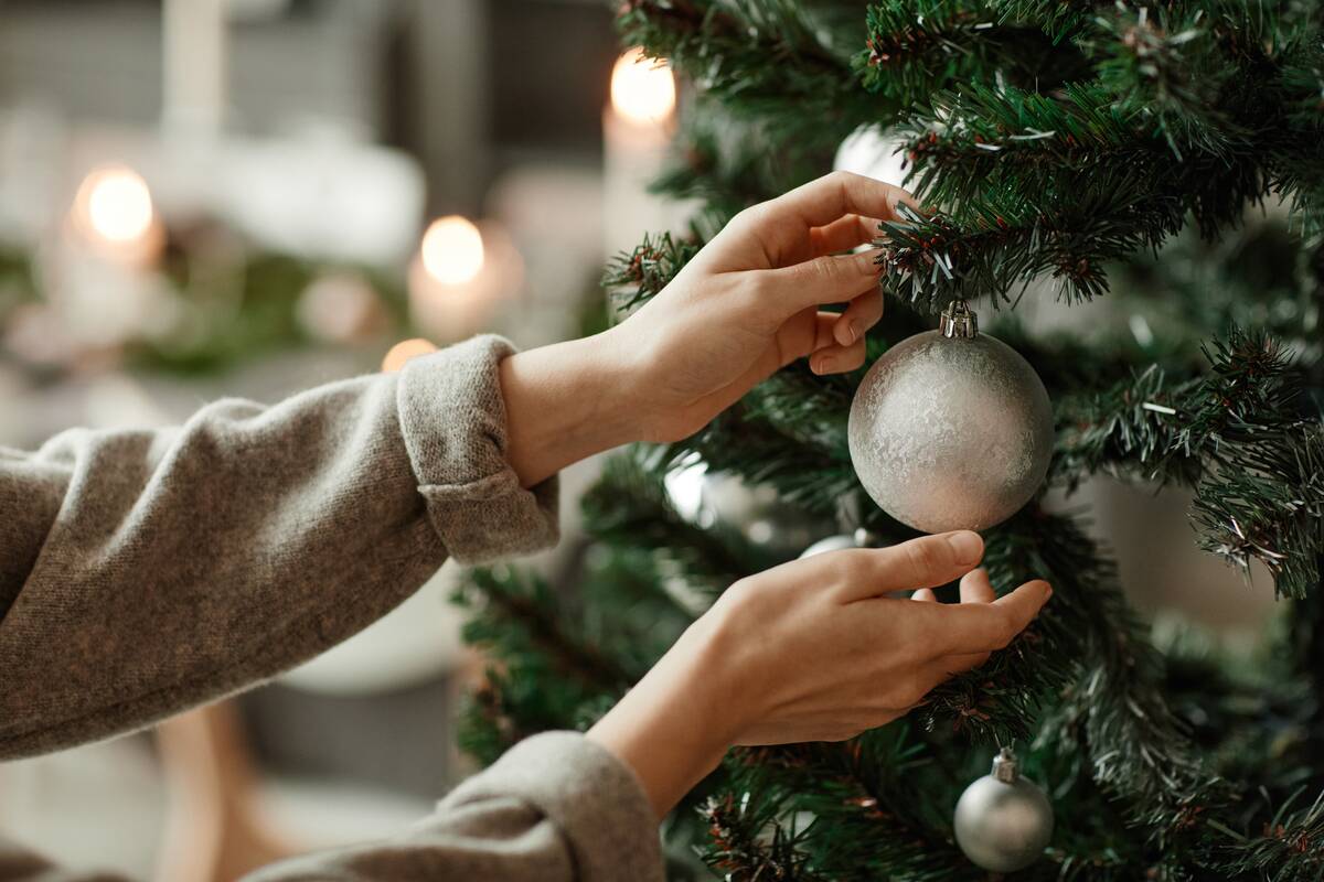 Side view close up of young woman decorating Christmas tree at home with silver ornament.