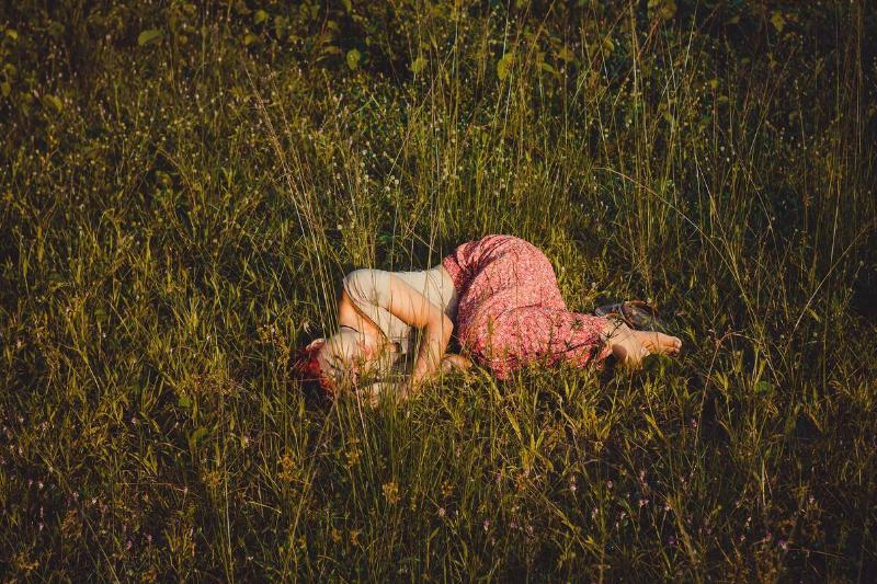 A woman curled up, resting in a grassy field.