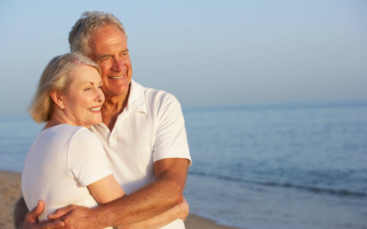 An older couple embracing while standing on a beach.
