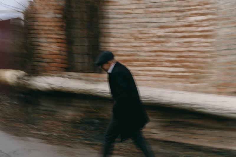A British 'mafia type' dressed man walking down a street, the image slightly blurred