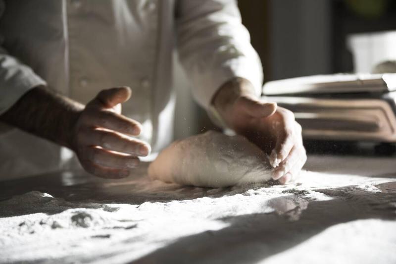 A pizza chef kneading a ball of dough on a floured counter top