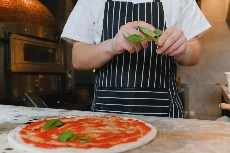 A pizza chef putting basil leaves on a pizza