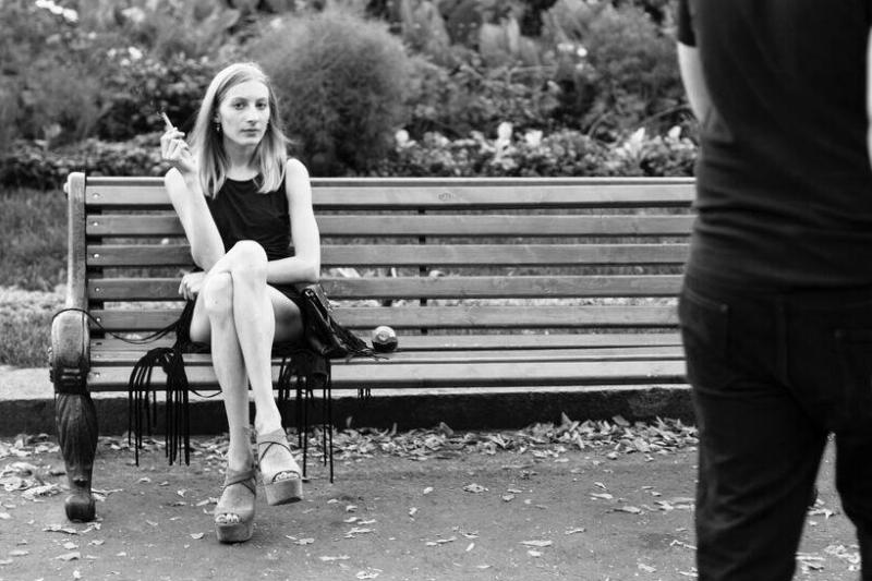 A woman on a bench with a cigarette in her hand looking at the camera judgementally.