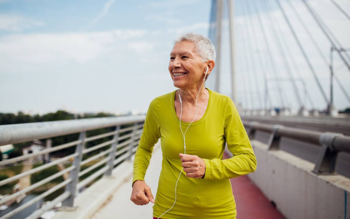 A woman smiling as she's out for a run, ina  bright yellow shirt and with wired earbuds in.