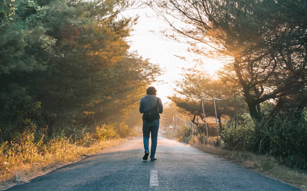 A man walking down a road, facing the sun.