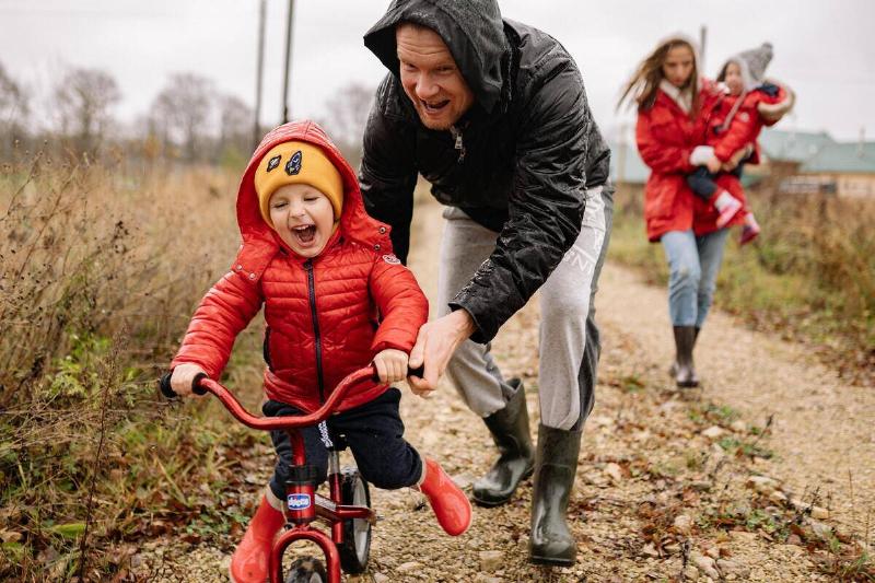 child in red raincoat on bicycle being pushed by dad