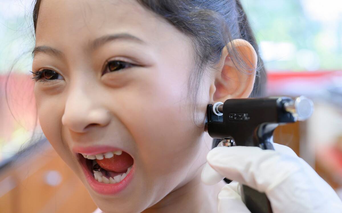 A young girl yelling as she gets her ear pierced with a piercing gun.
