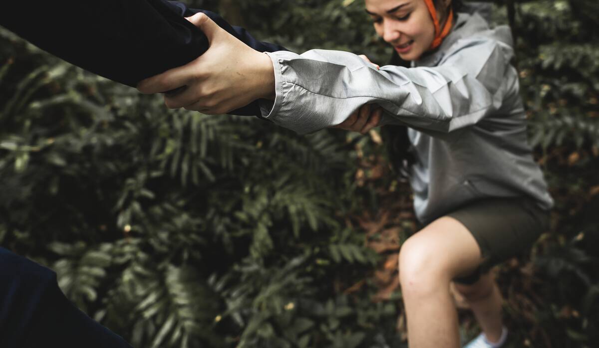 Someone helping another person of a large step while hiking.