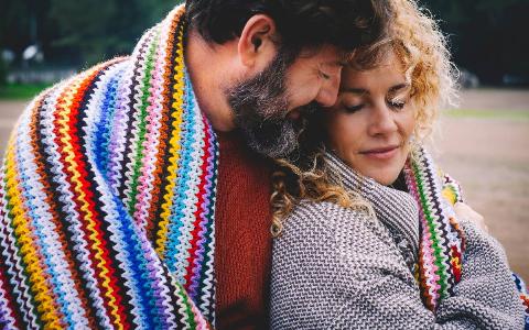 Romantic adult couple hugging while covered by a woolen colorful blanket at the outdoor park.