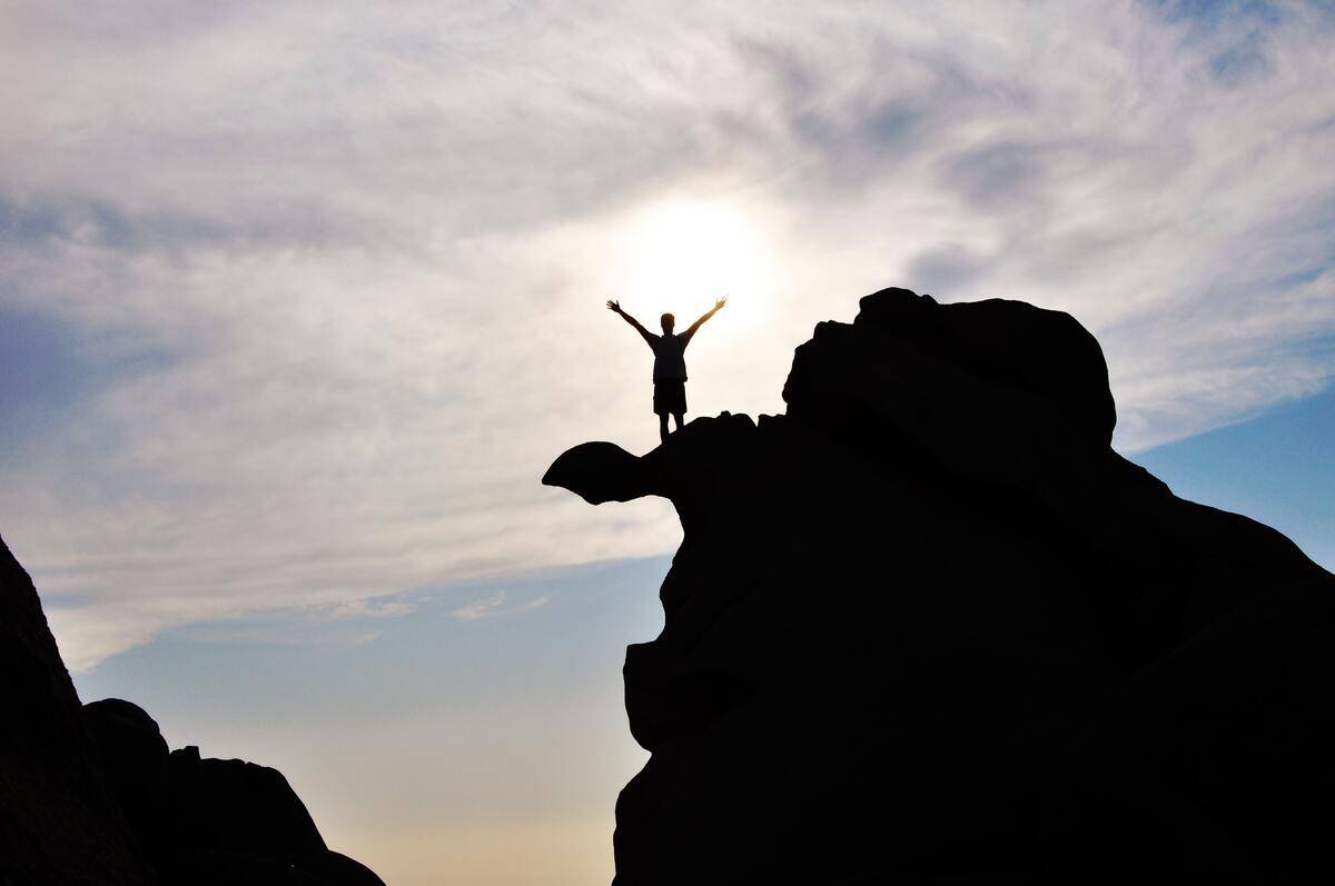 A silhouette of someone raising their arms after scaling a rock face.