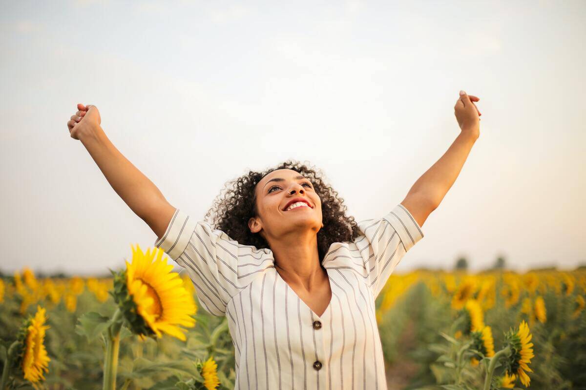 A woman standing among a field of sunflowers, raising her arms.