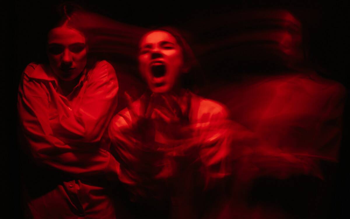 A woman lit in red in pain, blurry versions of herself swirling on either side.