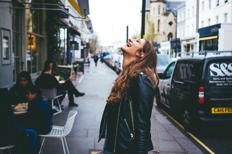 woman in black leather jacket on street smiling up at sky