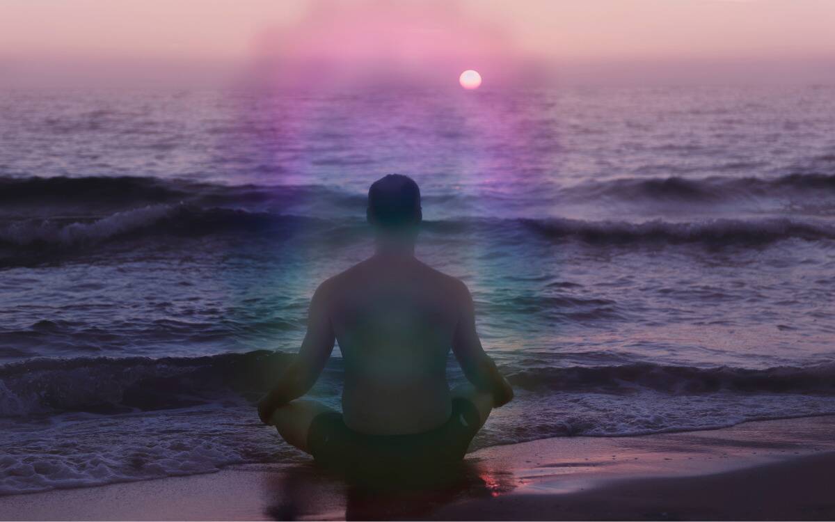 A man sitting on a beach with a colorful aura glowing around him.