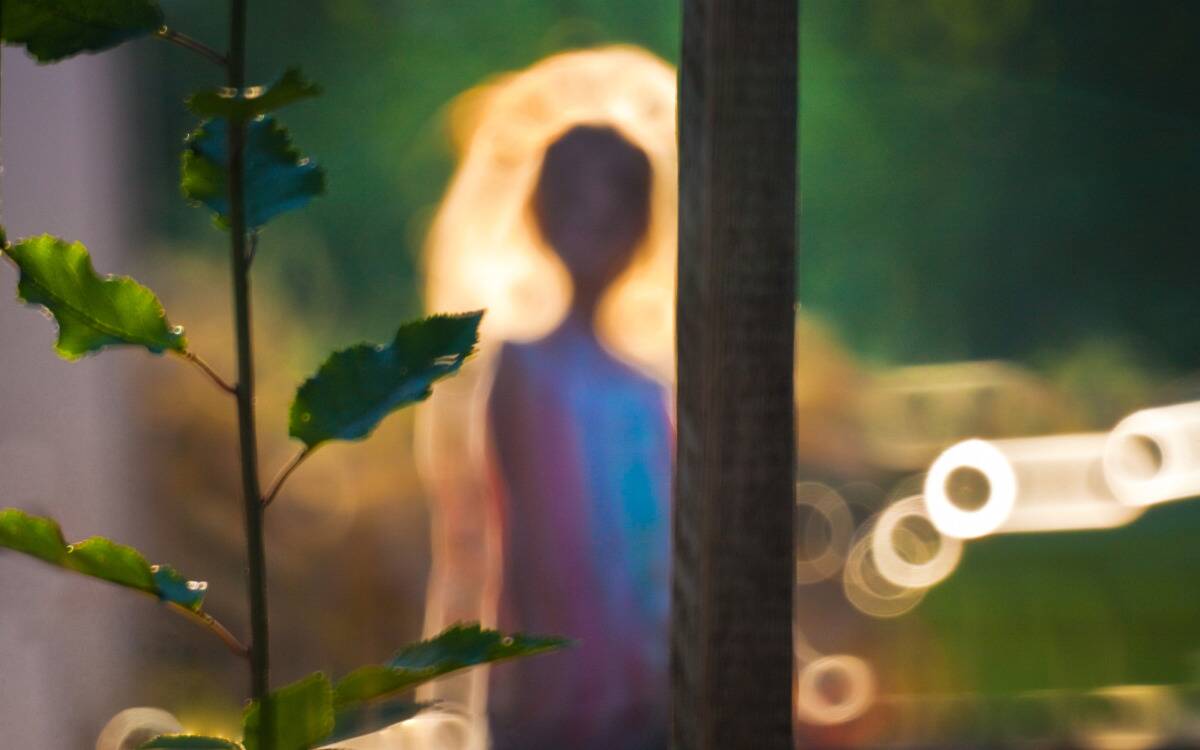 A blurry photo of someone through a window. The sunlight is casting a yellow aura around their silhouette.