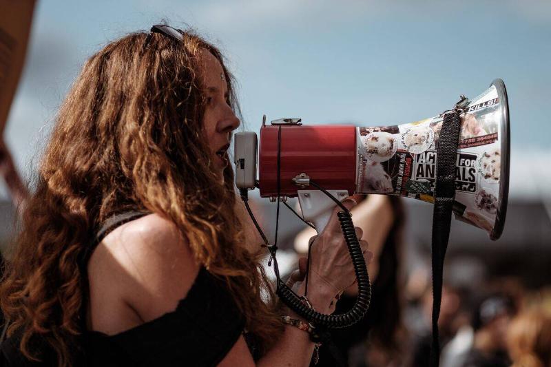 woman at protest outdoors speaking into megaphone covered in stickers