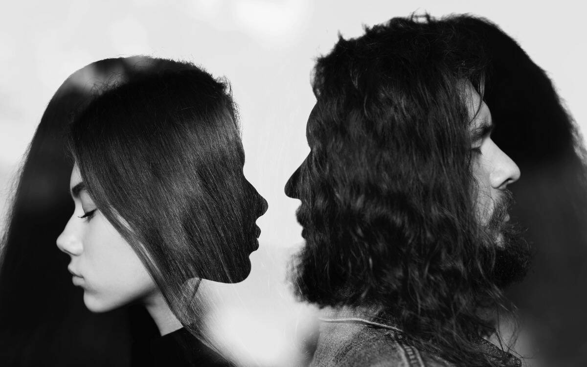 A silhouette of two people facing one another, while in the silhouettes their actual faces are turned away.