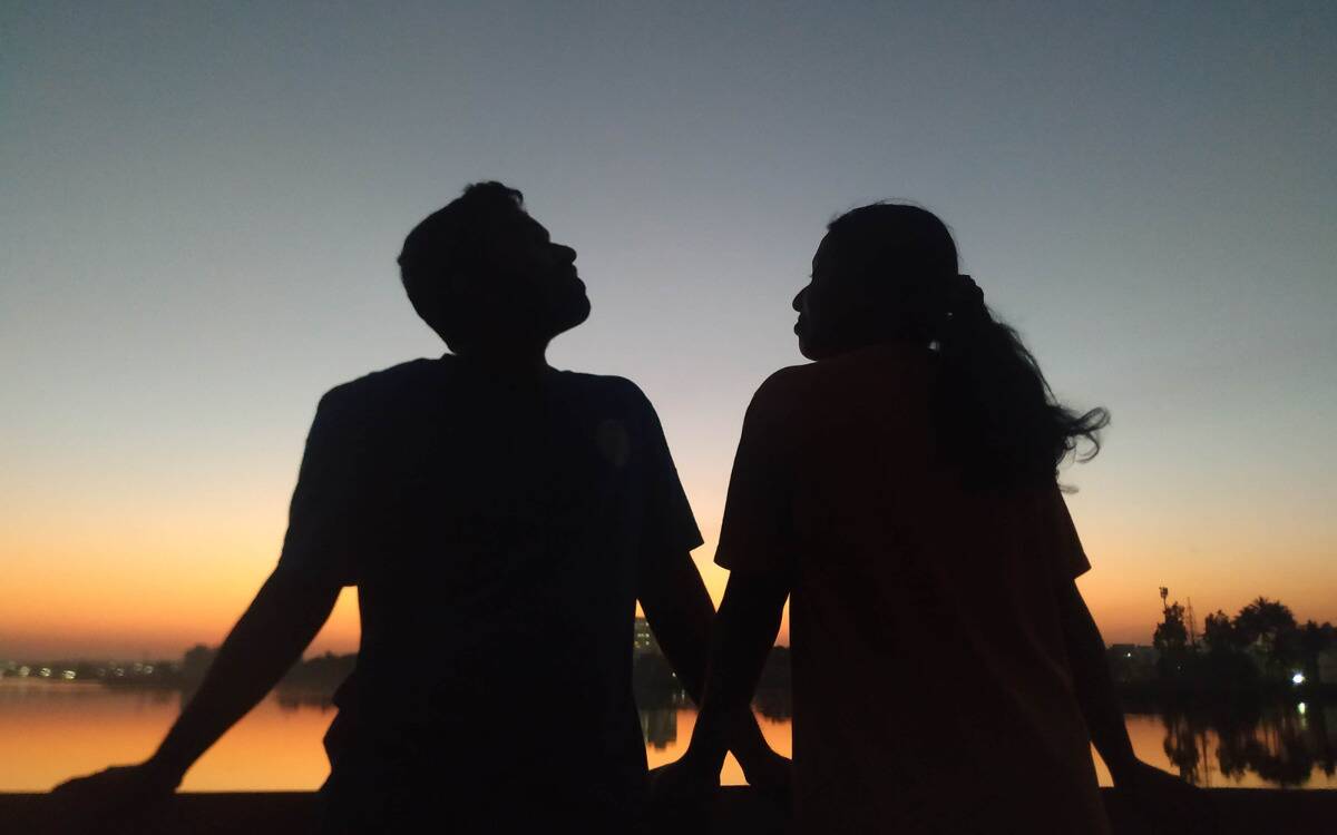 A silhouette of a couple seated next to each other in front of a lake.