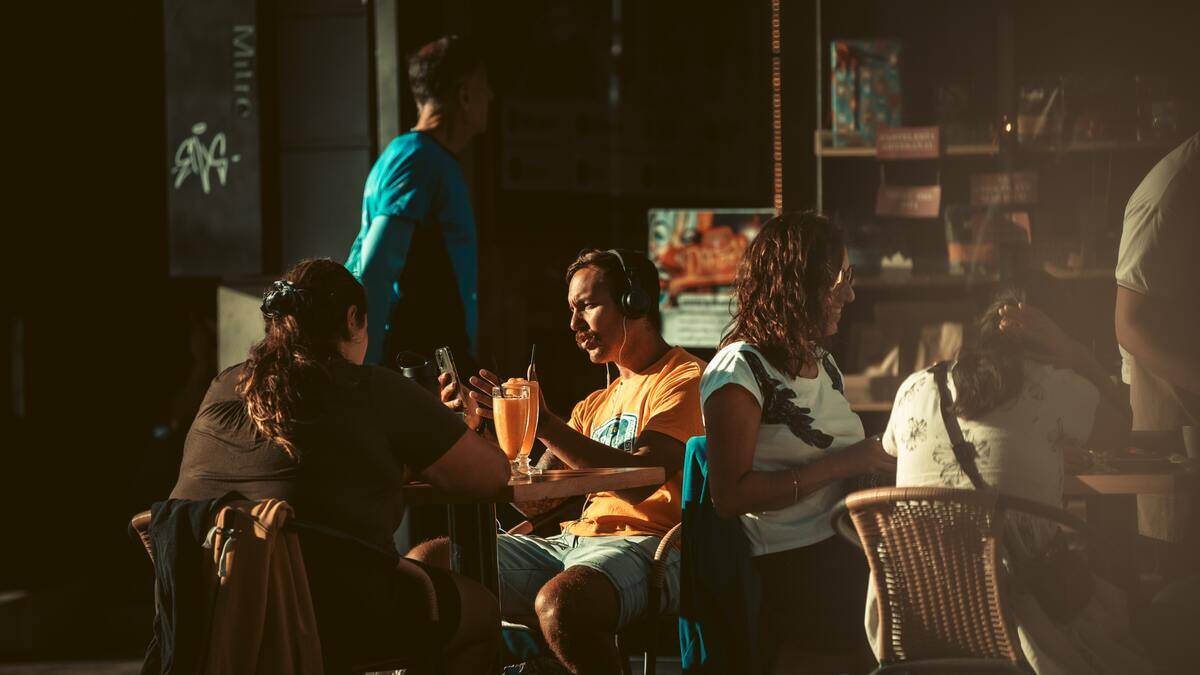 People sitting at tables outside a cafe, talking.