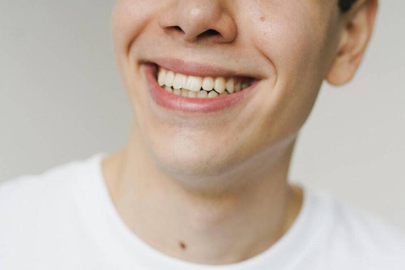 A closeup of a man in a white shirt smiling, focusing on the lower half of his face.