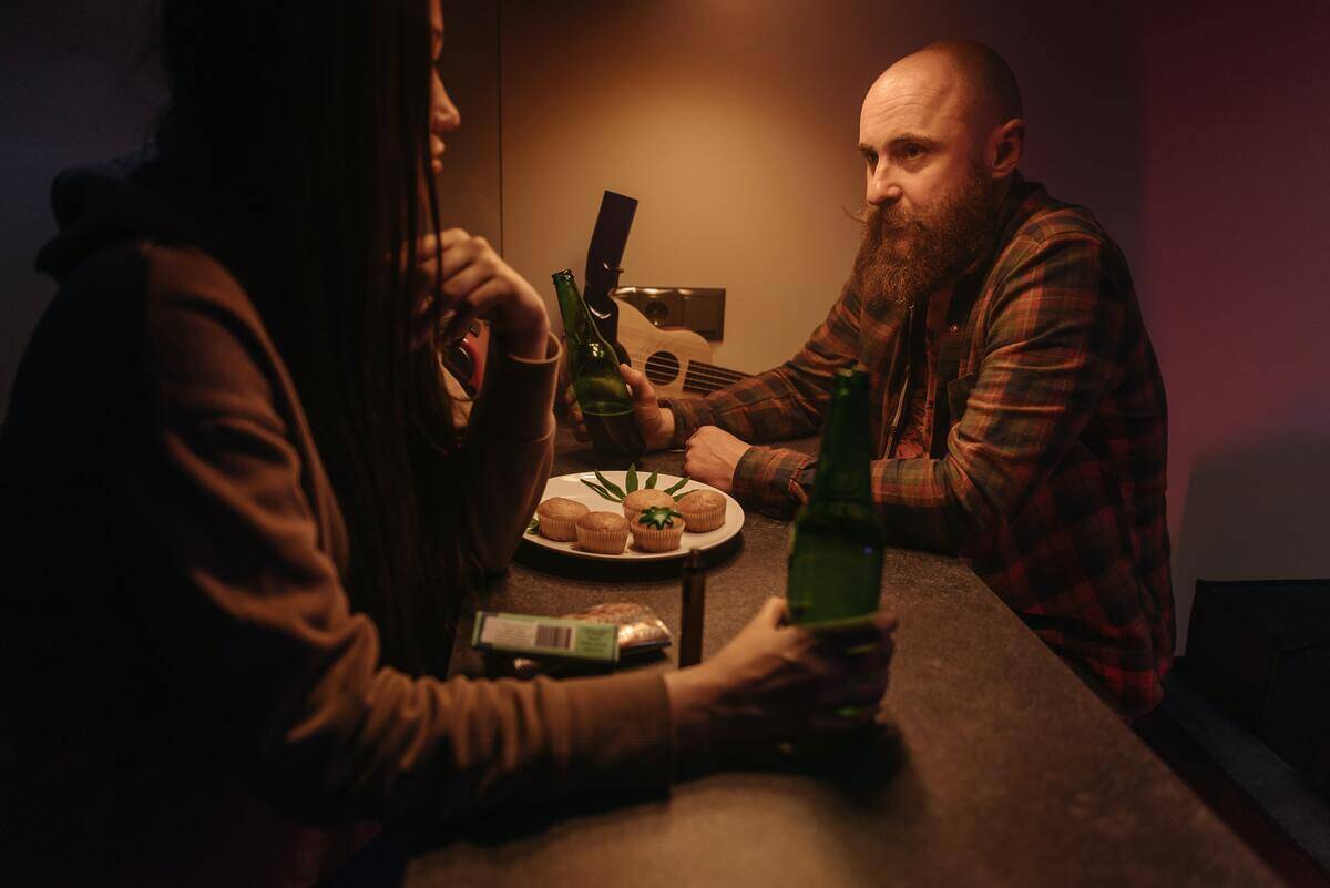 A man and a woman sitting at a counter, both holding a beer bottle.