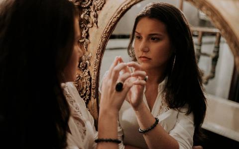 A woman looking in a mirror, oval with a gold frame.