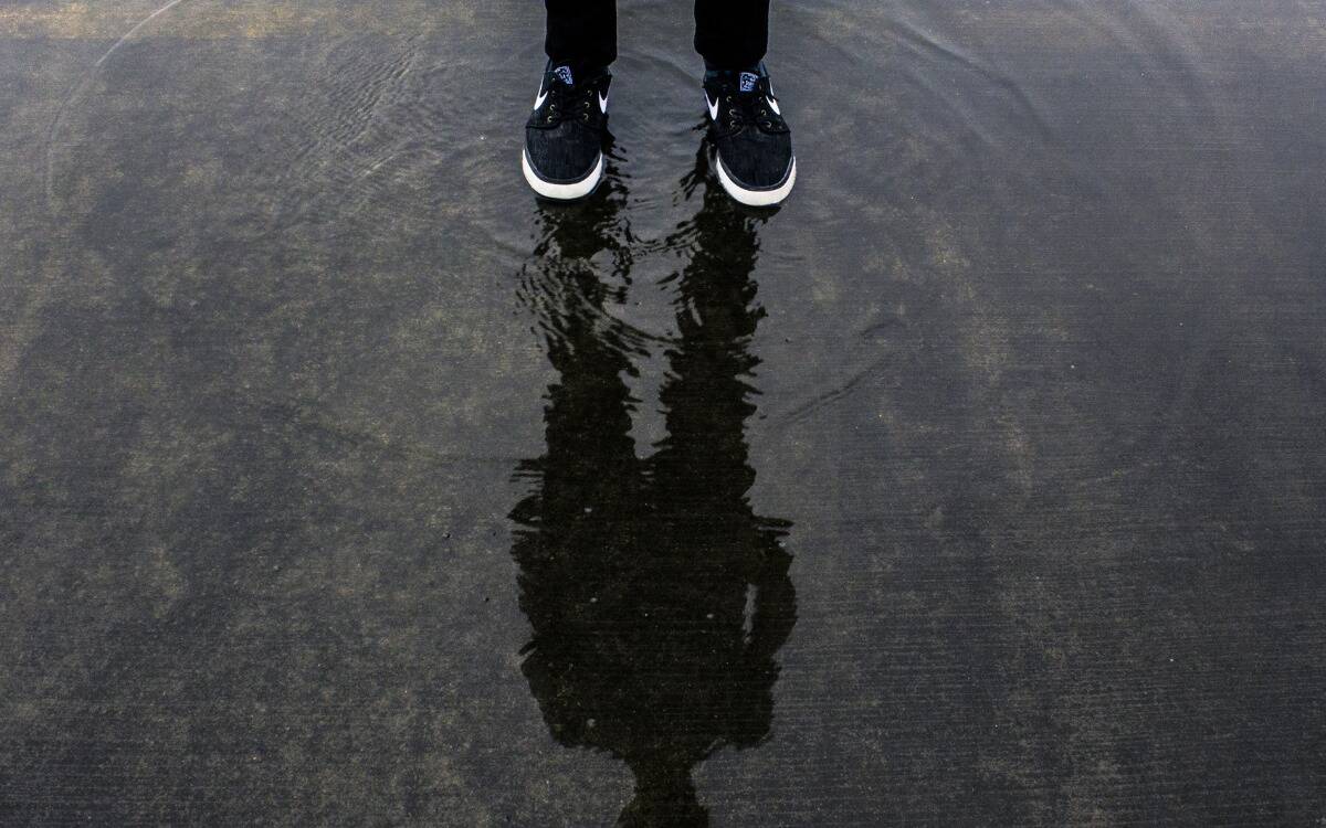 Someone standing in a puddle, the silhouette of their body visible in the reflection.