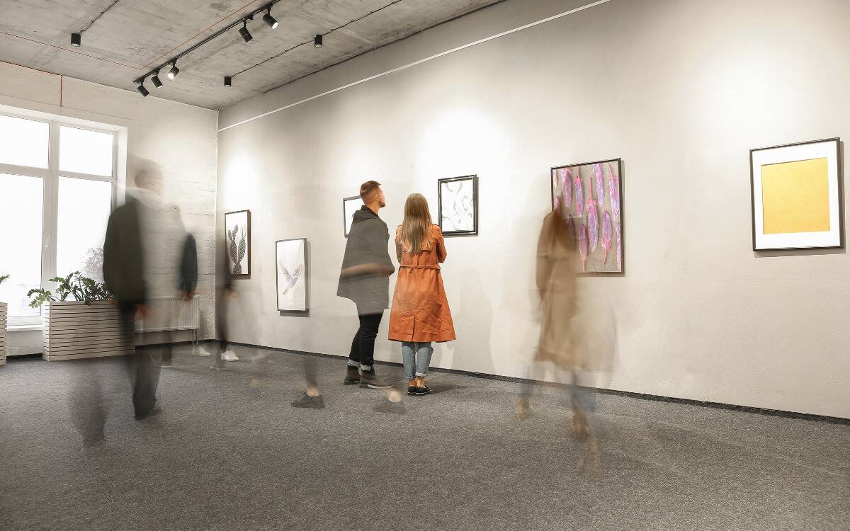 Two people standing in front of a painting at a gallery as the blur of people more aronud them.
