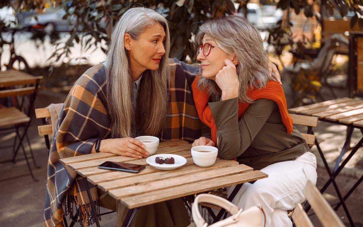 Two older woman sitting at a table, listening to one another.