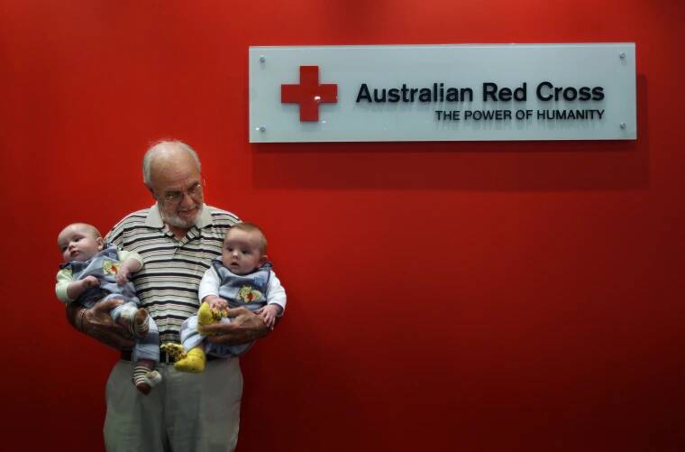 James standing by the Australian Red Cross sign holding two babies his blood helped save.