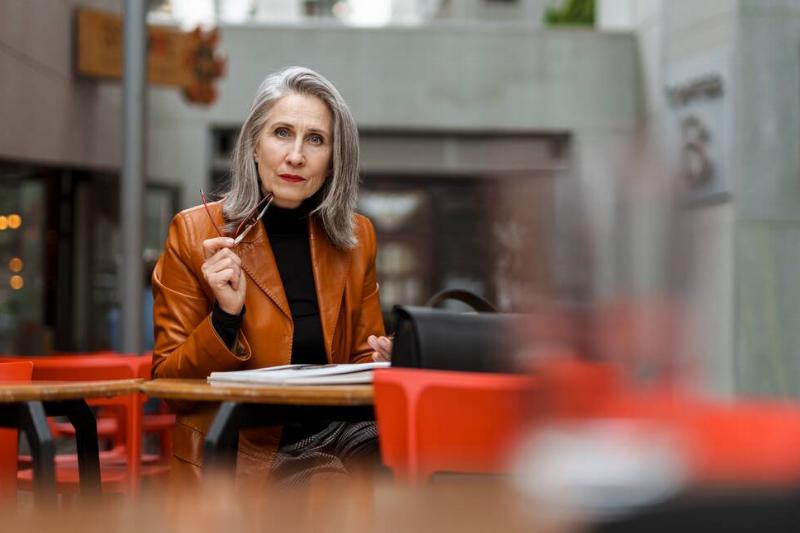 Woman with grey hair reading book while sitting in cafe outdoors.