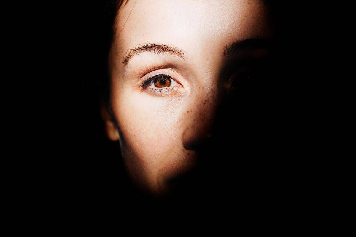 A portrait of a woman with only half her face in light, focusing on her eye.