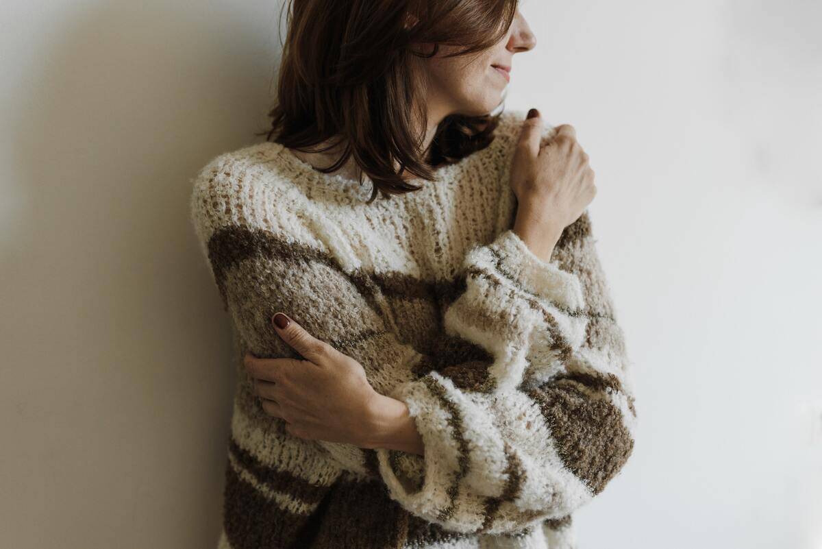 A woman in a brown sweater hugging herself.