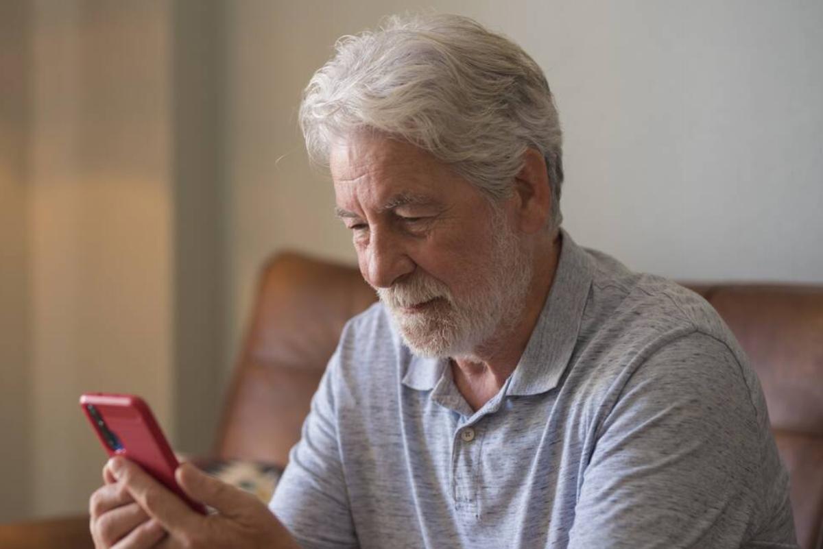 An older man reading his cellphone while sitting on a couch.