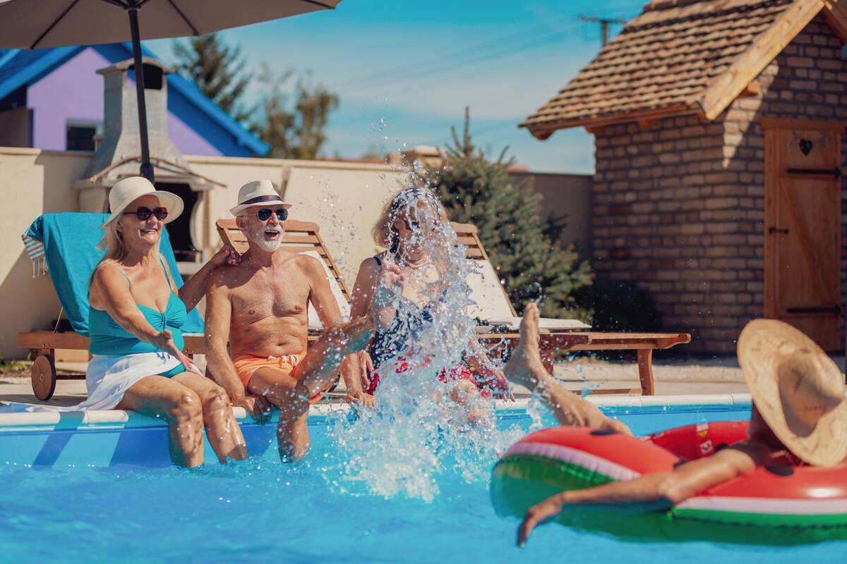 Group of elderly people having fun spending hot sunny summer day at the swimming pool, sunbathing and splashing water on each other.