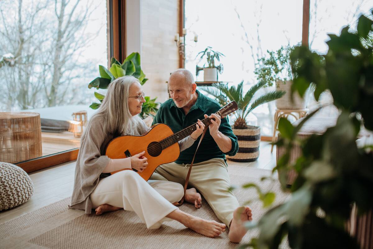 Senior couple playing on guitair, sitting in a cozy living room and enjoying autumn day.