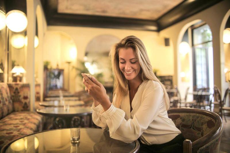 blonde woman smiling holding phone sitting in empty restaurant
