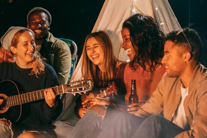 group of friends sitting around the fire laughing with guitar