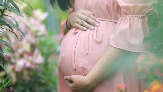 A pregnant woman in a pink dress caressing her stomach while standing outside.