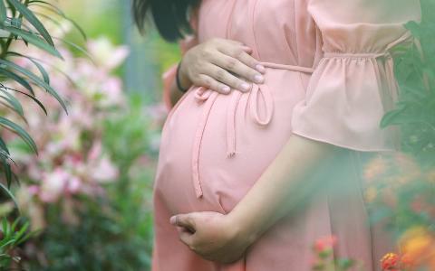 A pregnant woman in a pink dress caressing her stomach while standing outside.