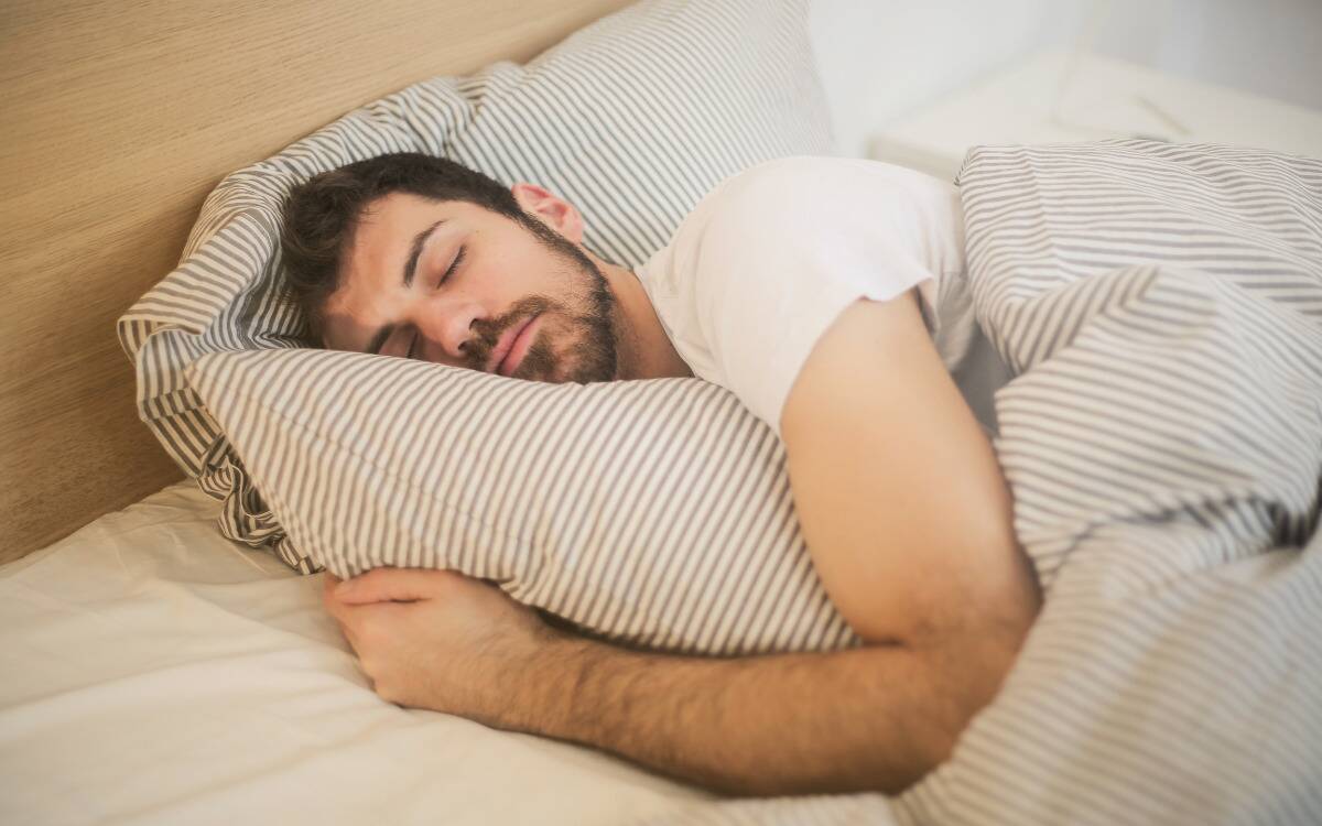 A man asleep while hugging a pillow on his bed.