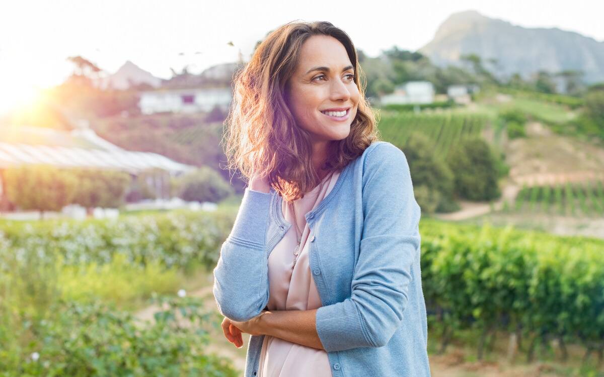 A woman standing outside and smiling off into the distance.