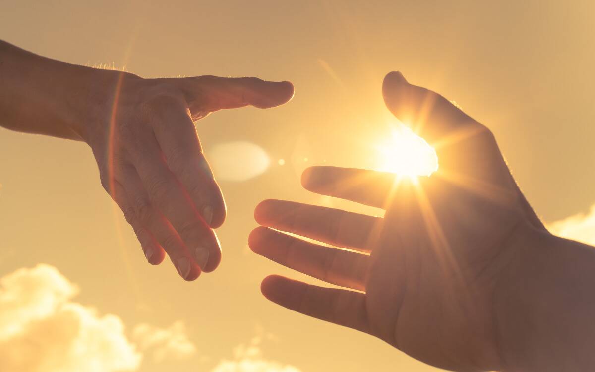 Two hands reaching out toward one another in the sunlight.
