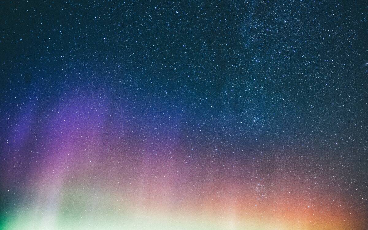 A sky full of stars with colorful aurora lights at the bottom.