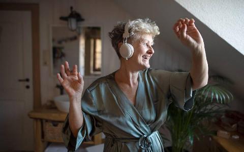 An older woman dancing by herself in her room, wearing headphones and a silk robe.