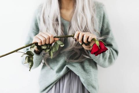 Woman with dyed grey hair holding a red rose.