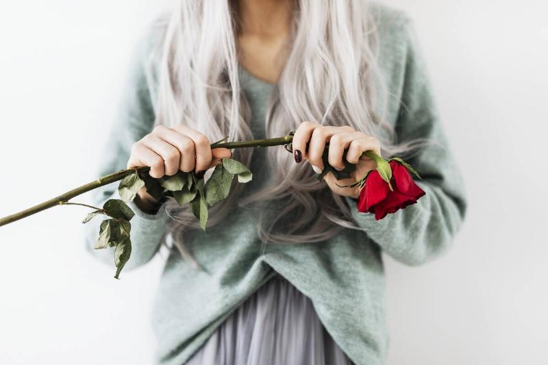 Woman with dyed grey hair holding a red rose.