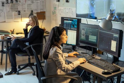 Woman sitting at a desk with multiple monitors, conducting serious work.
